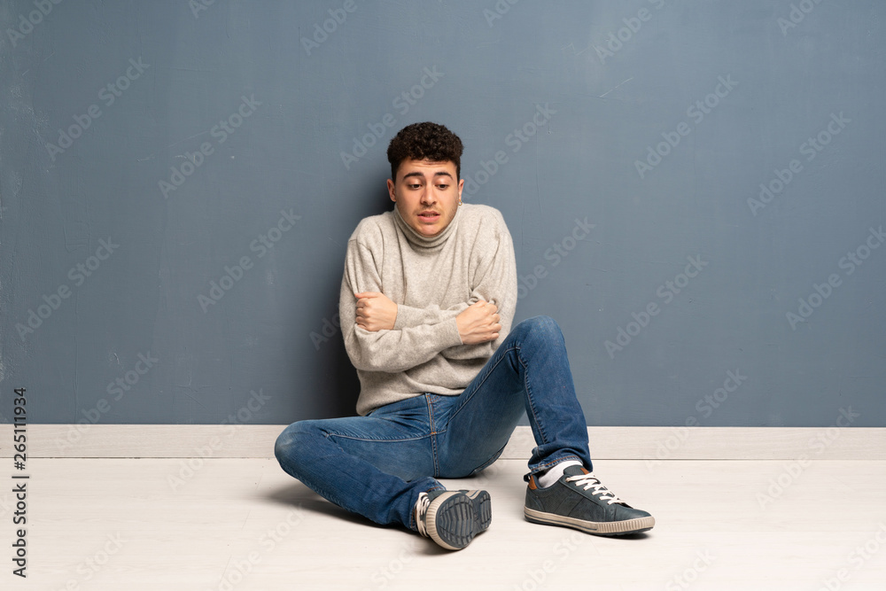 Young man sitting on the floor freezing Young man sitting on the floor freezing