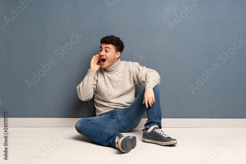 Young man sitting on the floor shouting with mouth wide open to the lateral