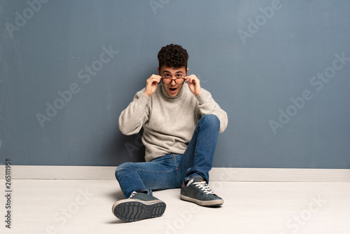 Young man sitting on the floor with glasses and surprised