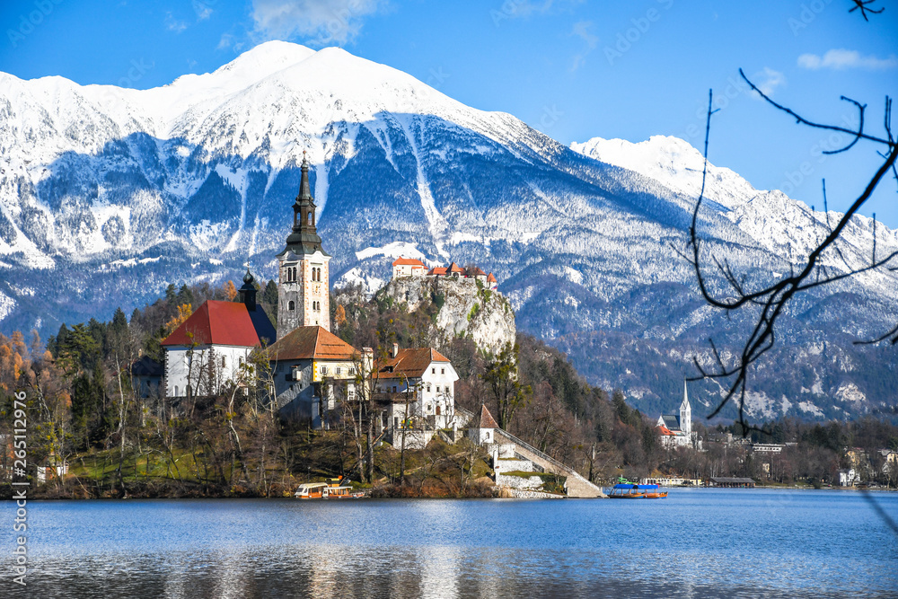 Small natural island in the middle of alpine lake with church dedicated to assumption of Mary and castle with snowy mountain range in the background in winter landscape Bled, Slovenia