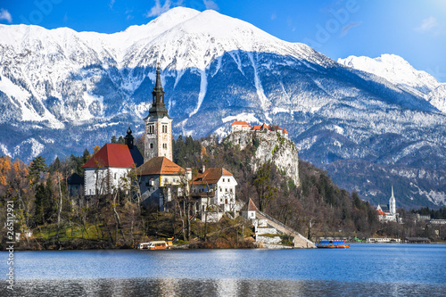 Small natural island in the middle of alpine lake with church dedicated to assumption of Mary and castle with snowy mountain range in the background in winter landscape Bled, Slovenia