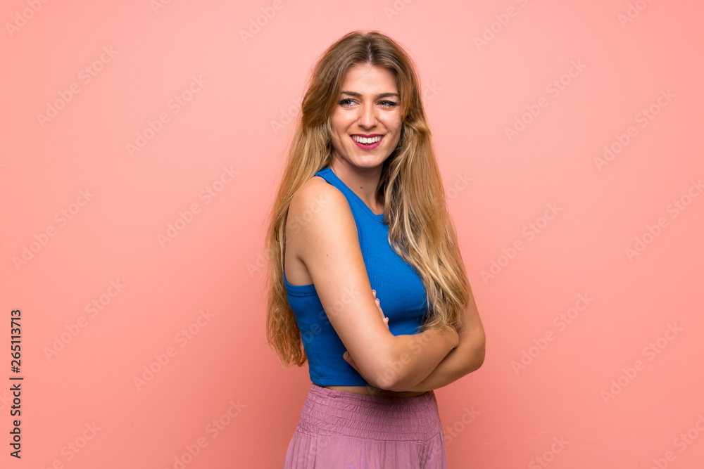 Young blonde woman over isolated pink background with arms crossed and happy