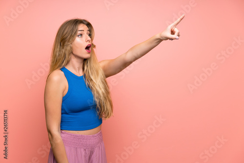 Young blonde woman over isolated pink background pointing away