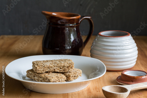 Breakfast cereal bars in bowl, with milk and honey jar in background