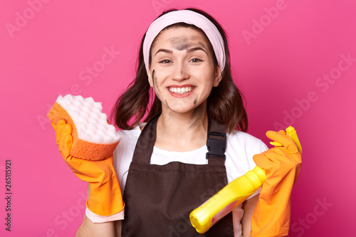 Cheerful energetic bright young woman looks happy isolated over pink background in studio, ready to do general cleaning, stain her face while tiding up, wearing working clothes. Household concept. photo