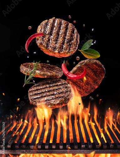 Beef milled meat on hamburger with spices fly over the flaming grill barbecue fire.