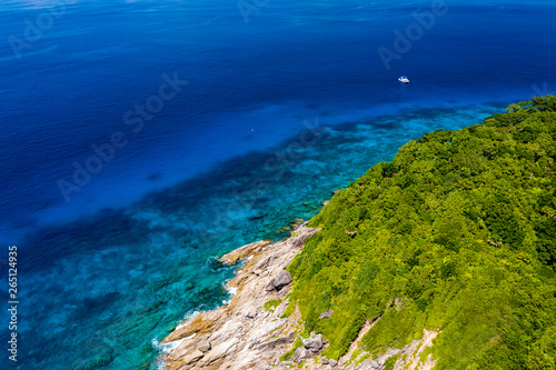 Aerial drone view of a lush tropical island with crystal clear water surrounded by coral reef