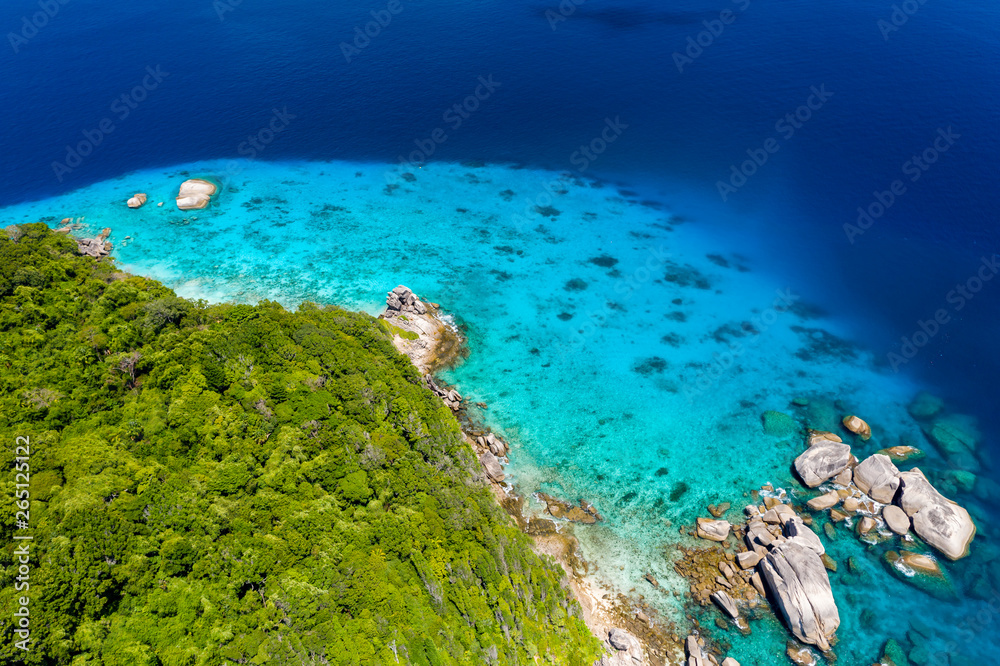 Aerial drone view of a lush tropical island with crystal clear water surrounded by coral reef
