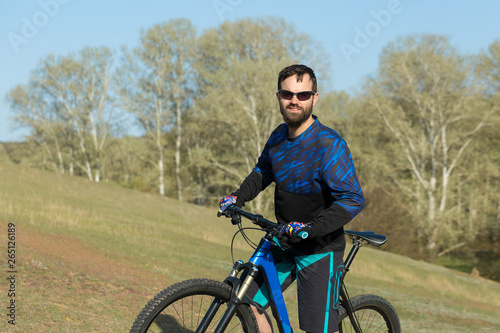 Fototapeta Naklejka Na Ścianę i Meble -  Cyclist in shorts and jersey on a modern carbon hardtail bike with an air suspension fork rides off-road on green hills near the forest