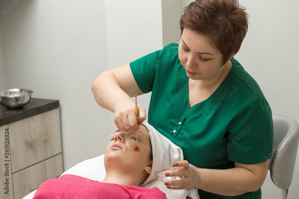 Face skin care. Beautician applying beauty oil mask on face using brush In spa salon	