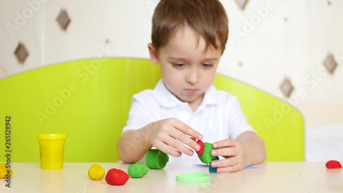 The child is having fun at the table, close-up, playing in the multi-colored modeling of plasticine or dough for games photo