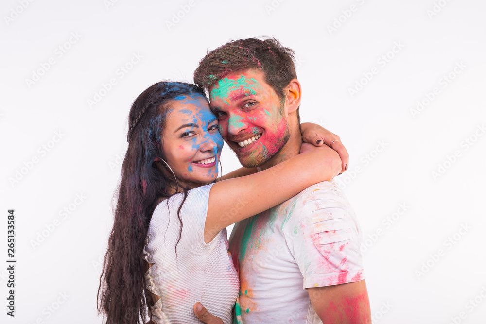Holiday, holi and people concept - Smiling funny woman and man posing with multicolored powder on their faces on white background Holiday, holi and people concept - Smiling funny woman and man posing with multicolored powder on their faces on white background