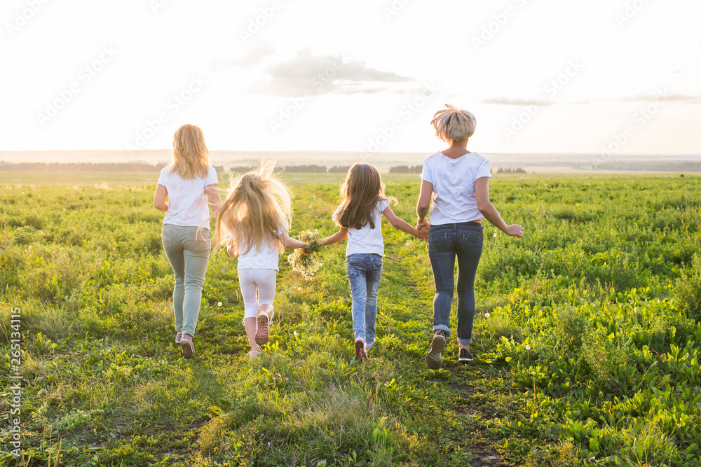 Family, summer and holiday concept - Group of women and girls going away in green field Family, summer and holiday concept - Group of women and girls going away in green field