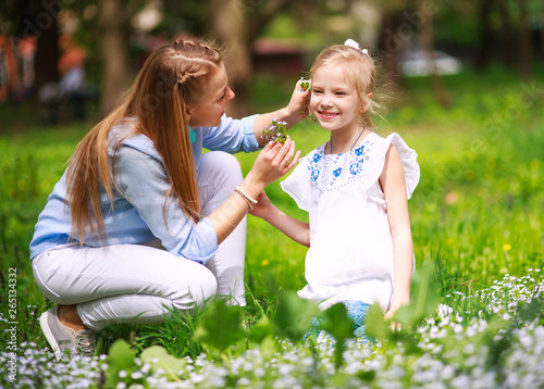 Mother with daughter in green blooming summer park on meadow collect flowers