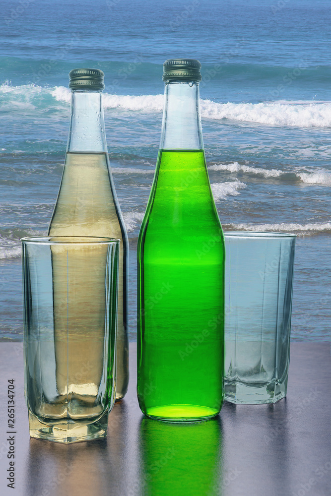 bottles of refreshing lemonade and wine glasses against a blue sea bottles of refreshing lemonade and wine glasses against a blue sea