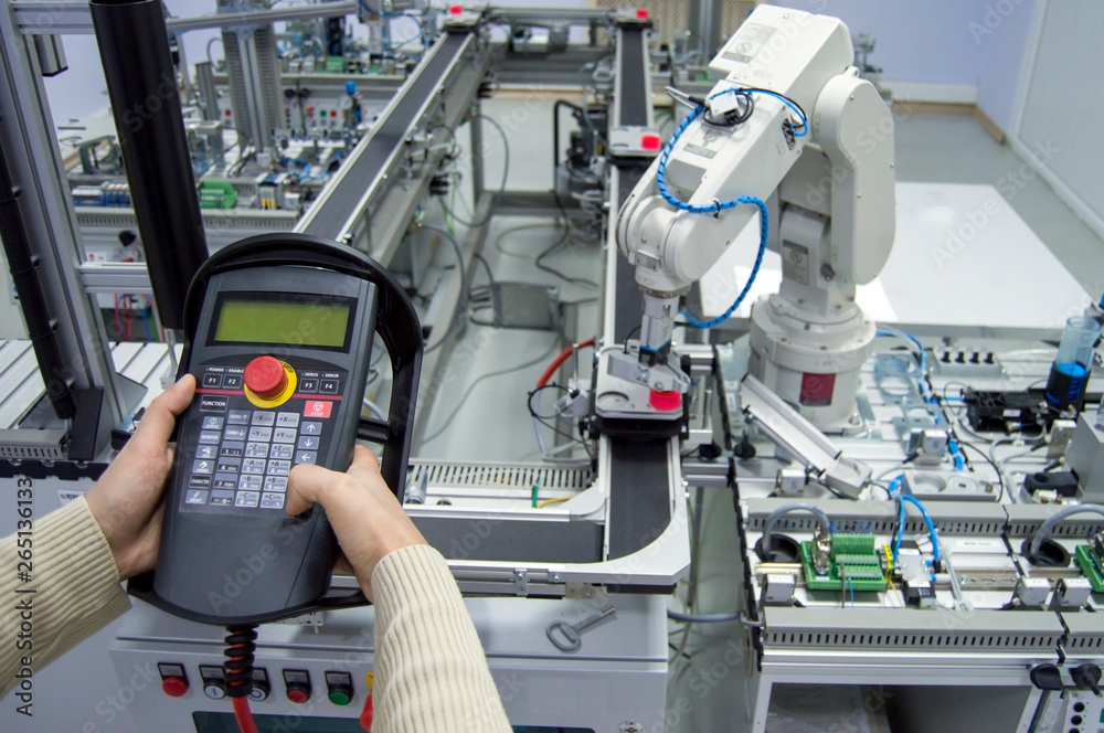 Man is pushing button on teach panel to control a robotic arm which is integrated on smart factory production line. industry 4.0 automation line which is equipped with sensors and robotic arm. Man is pushing button on teach panel to control a robotic arm which is integrated on smart factory production line. industry 4.0 automation line which is equipped with sensors and robotic arm.