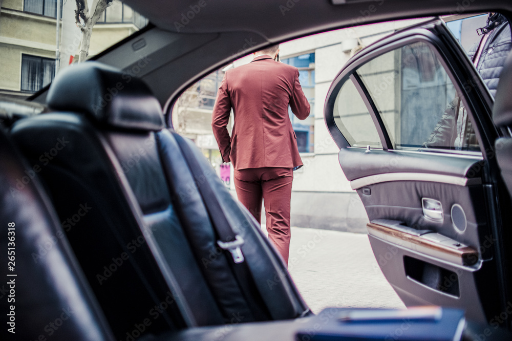 Young businessman talking on cell phone and standing near the limo with an open door Young businessman talking on cell phone and standing near the limo with an open door