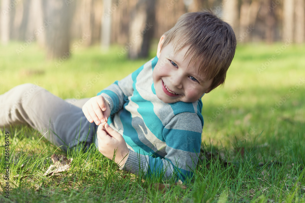 A little boy is smiling and lying on the green grass in the park. A little boy is smiling and lying on the green grass in the park.