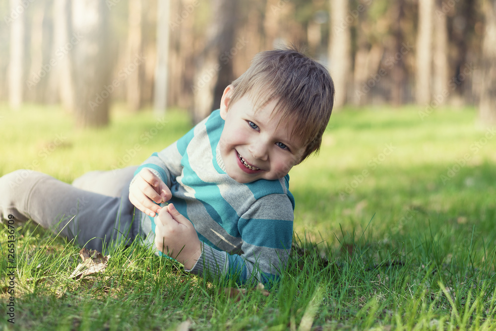 A little boy is smiling and lying on the green grass in the park. A little boy is smiling and lying on the green grass in the park.