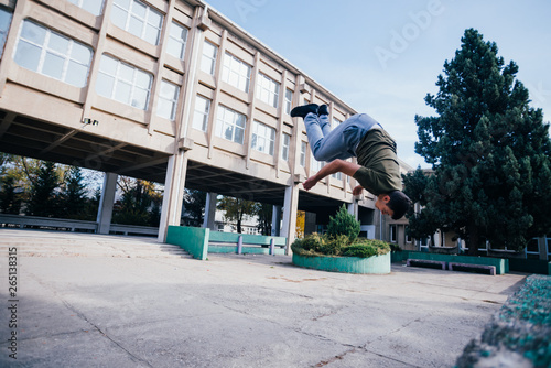 Athletic Parkour guy doing backflip and tricks while jumping off and over .a concrete wall. © qunica.com