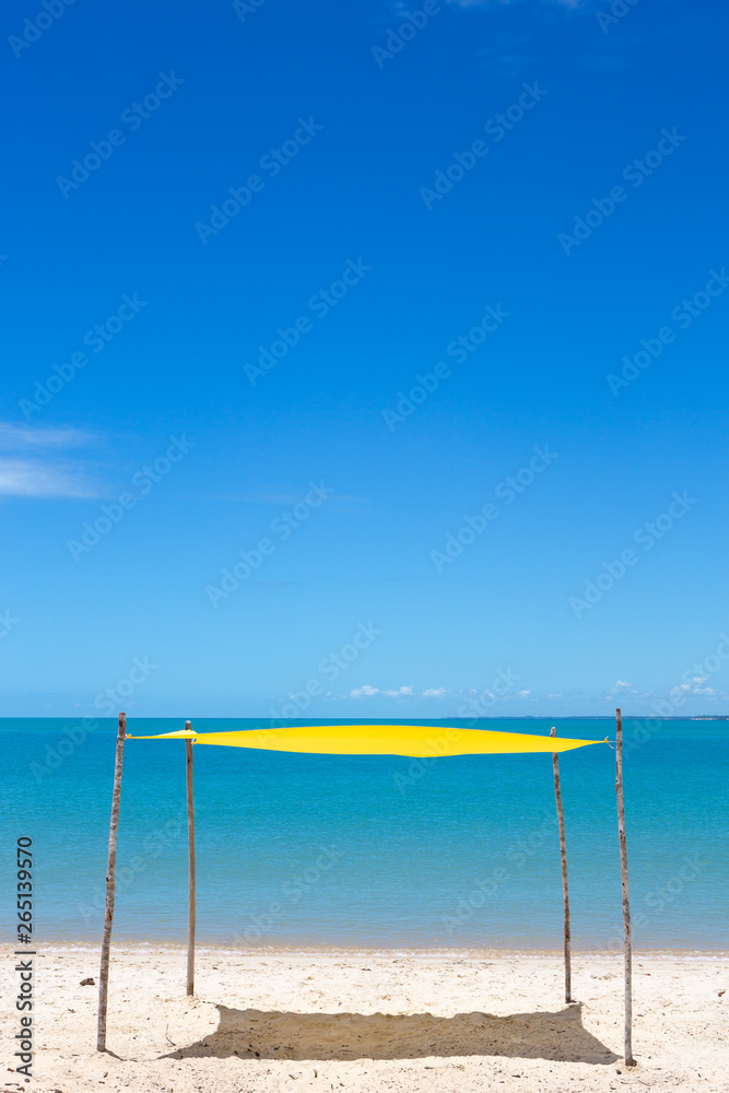 Beautiful beach view with a yellow tent on sunny summer day and sea and blue sky in the background. Concept of vacations, peace and relaxation. Ponta do Corumbau, Bahia, Brazil. Beautiful beach view with a yellow tent on sunny summer day and sea and blue sky in the background. Concept of vacations, peace and relaxation. Ponta do Corumbau, Bahia, Brazil.