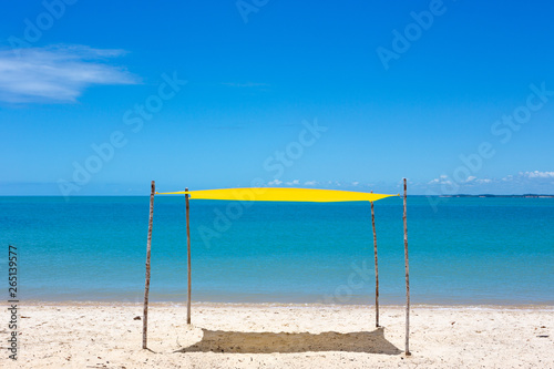Beautiful beach view with a yellow tent on sunny summer day and sea and blue sky in the background. Concept of vacations, peace and relaxation. Ponta do Corumbau, Bahia, Brazil. photo