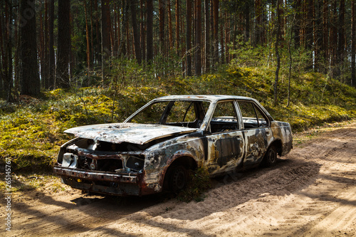 Fully burnt car in the forest in spirng on sandy road