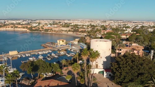 Drone flight over the tower of Cabo Roig and the boat harbor in the warm morning light on the Costa Blanca south of Torrevieja.