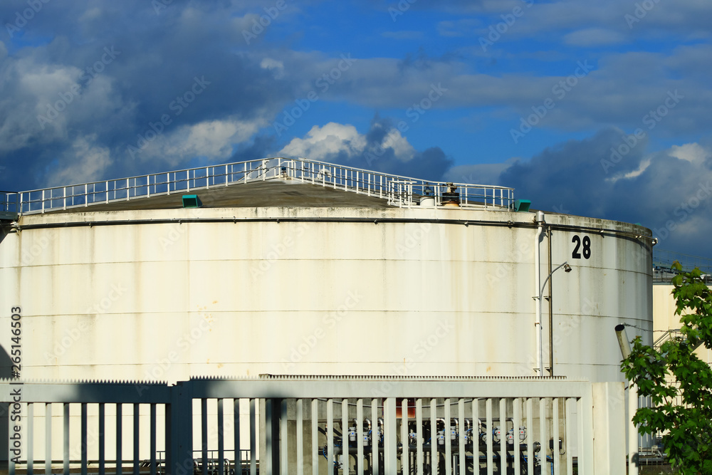 Fototapeta premium Numbered industrial water tank behind a metal barrier. Silo of a factory with its domed roof and its access bridge in a closed enclosure