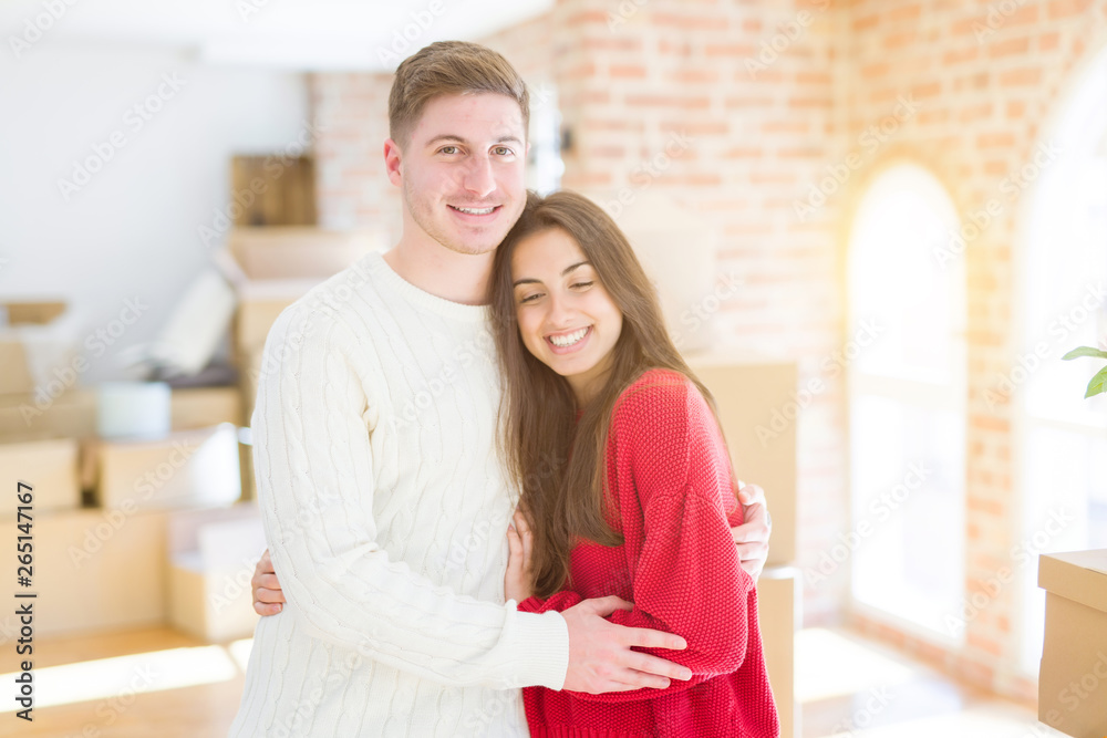 Beautiful young couple moving to a new home, standing on new aparment around cardboard boxes, hugging smiling happy and in love Beautiful young couple moving to a new home, standing on new aparment around cardboard boxes, hugging smiling happy and in love
