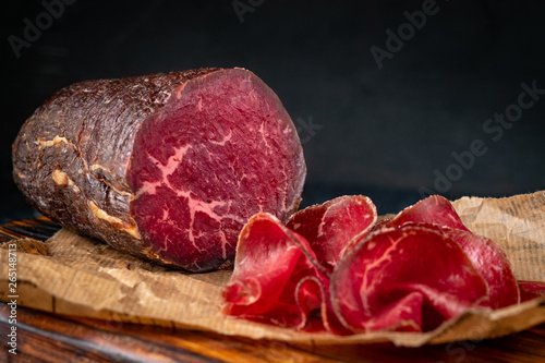 Half a smoked bresaola and cut pieces on a chopping Board. Italian Antipasti, rustic style photo