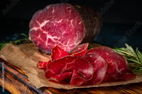 Half a smoked bresaola and cut pieces on a chopping Board. Italian Antipasti, rustic style photo