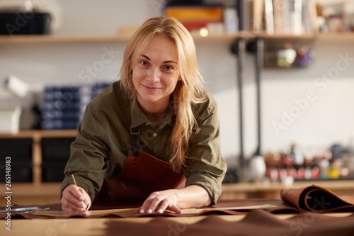 Portrait of female artisan smiling at camera while working with leather in workshop, copy space photo