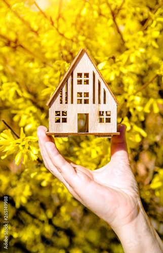 The girl holds the house symbol against the background of blossoming forsythia 