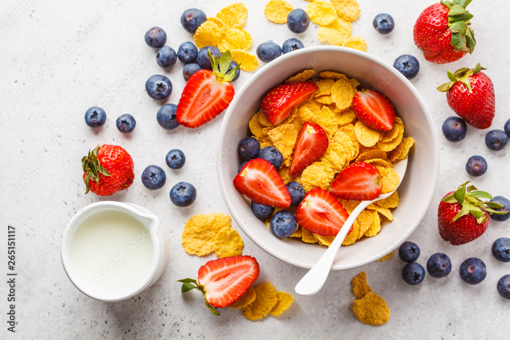 Cornflakes with strawberries and blueberries in a bowl on white background, top view. Cornflakes with strawberries and blueberries in a bowl on white background, top view.