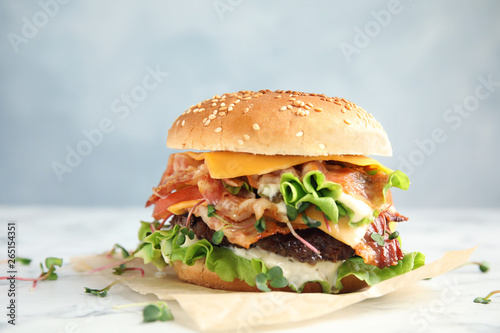 Tasty burger with bacon on table against color background photo