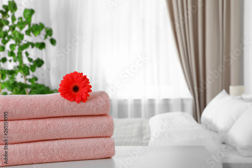 Stack of fresh towels with flower on table in bedroom. Space for text