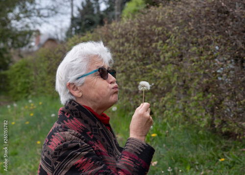Portrait of an elderly woman blowing on a dandelion flower in a park