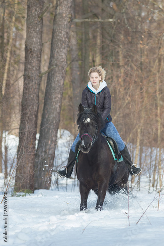 A young woman riding a black horse in the forest