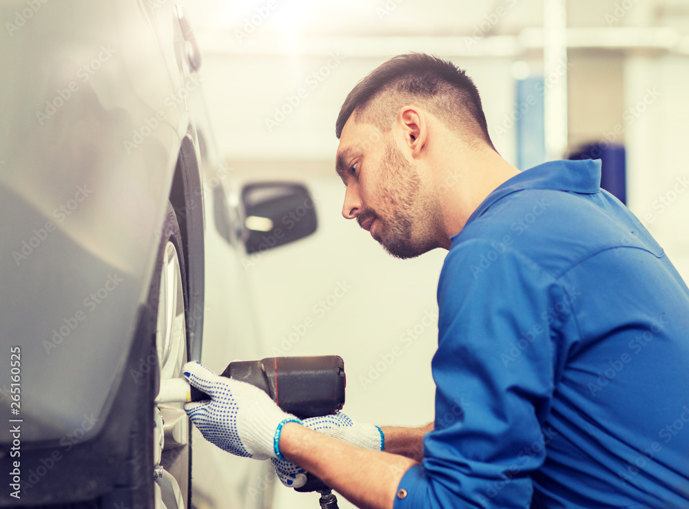 car service, repair, maintenance and people concept - auto mechanic man with electric screwdriver changing tire at workshop car service, repair, maintenance and people concept - auto mechanic man with electric screwdriver changing tire at workshop