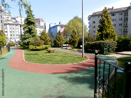 Park with pine trees and bushes in the city, apartments. Walking path.