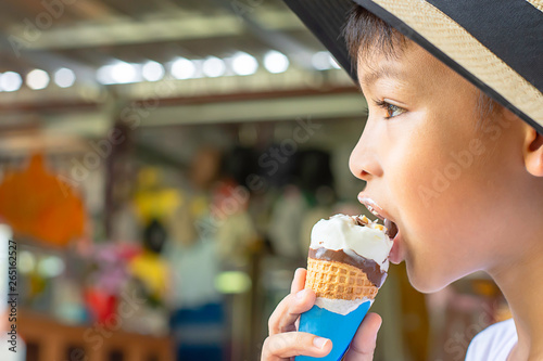 Asian Boys wearing a hat eating ice cream cone in hand.