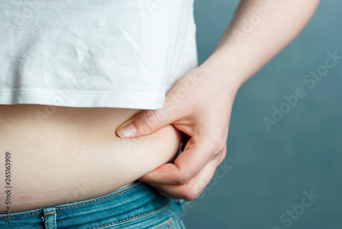 woman's hand holding excessive belly fat, the overweight concept