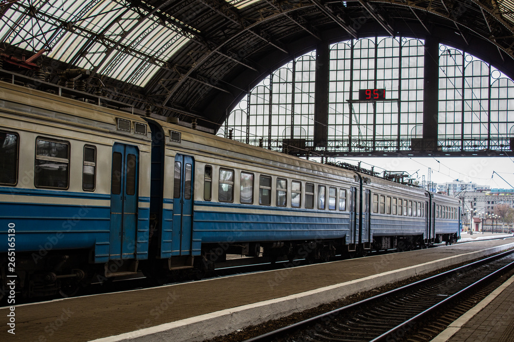 Blue cars of an electric train stopping under the roof of a covered apron of the railway station