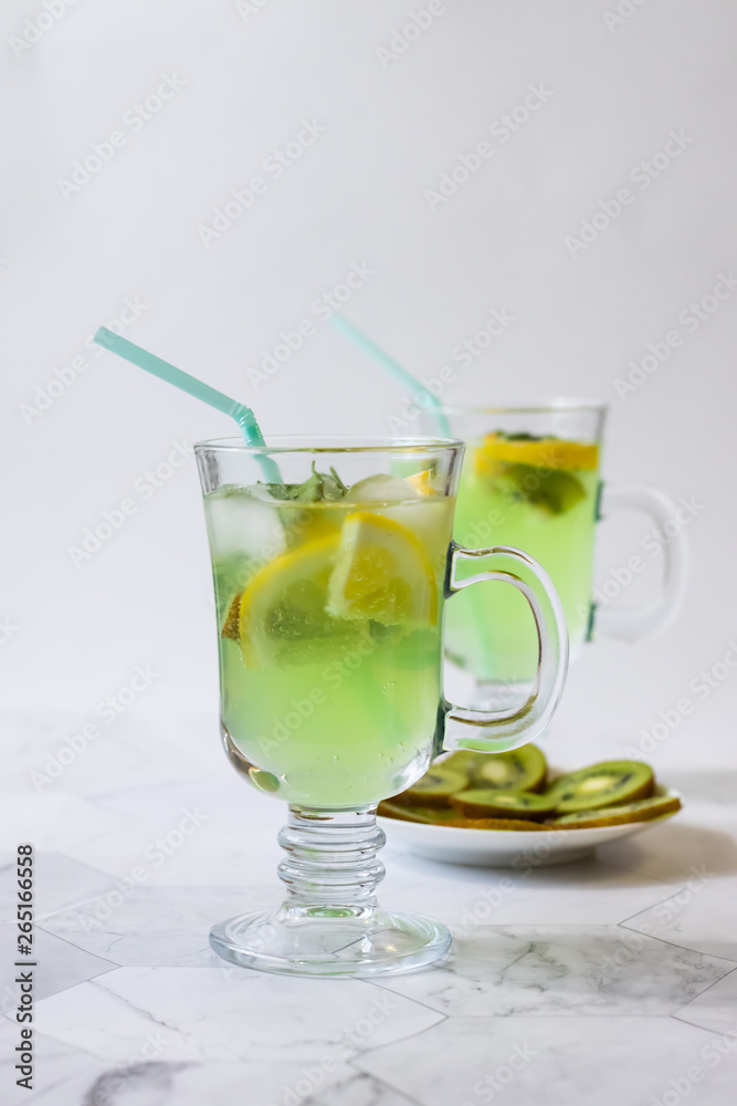Refreshing lemonade from kiwi and lemon with ice on a light background. Vertical orientation Refreshing lemonade from kiwi and lemon with ice on a light background. Vertical orientation