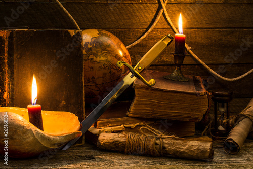 Tableau sur toile Old books and documents, a burning candle, globe and dirk stand on a wooden surface