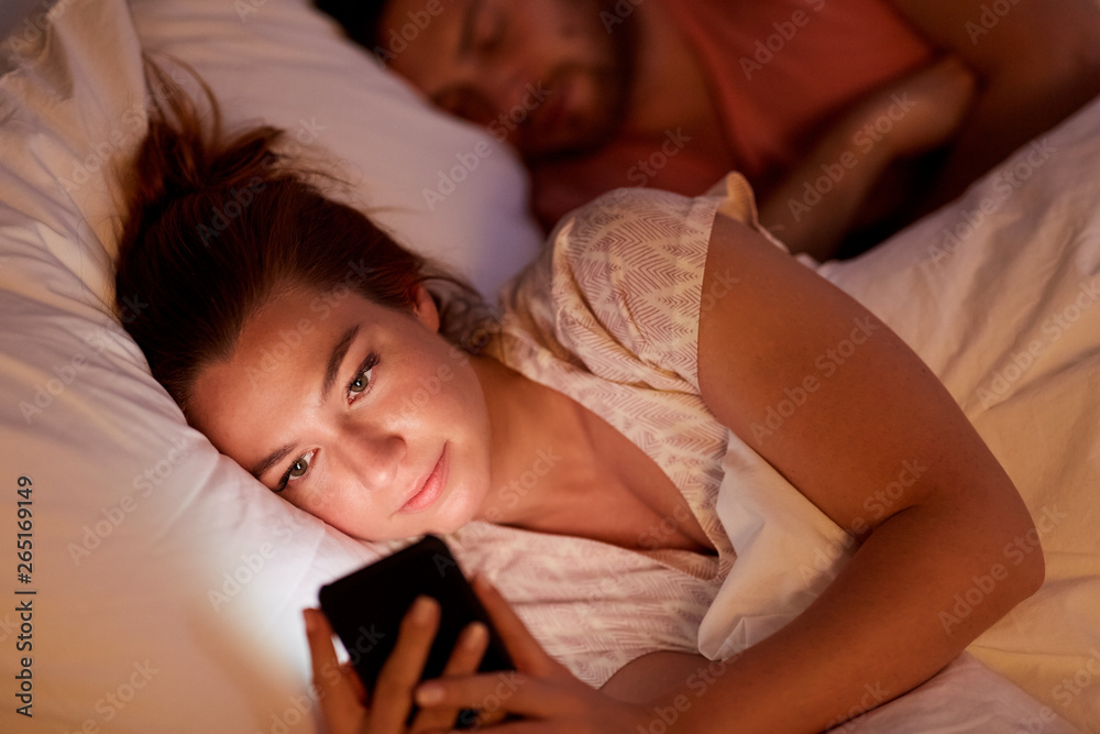 technology, internet addiction and cheat concept - woman using smartphone at night while her boyfriend is sleeping technology, internet addiction and cheat concept - woman using smartphone at night while her boyfriend is sleeping