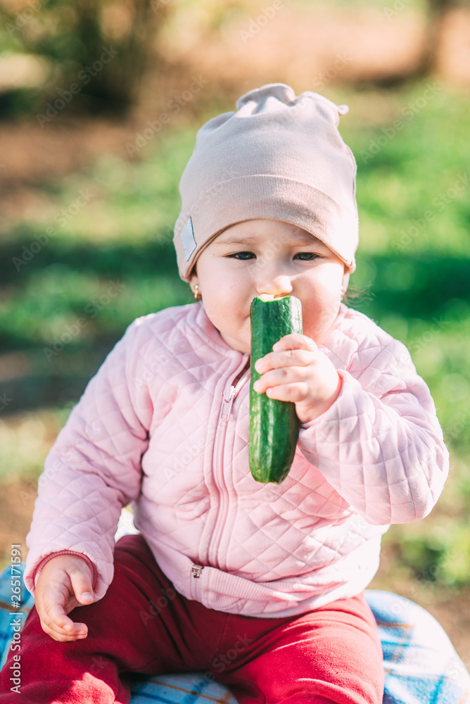 Funny little girl eating fresh cucumber in the garden in spring Funny little girl eating fresh cucumber in the garden in spring