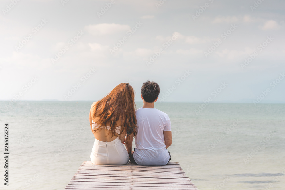 Back of view Vacations of romantic couple in love sitting on pier together seen beautiful sea and beach feeling so happiness and romantic in Tropical island in Thailand,Vacations or honeymoon Concept