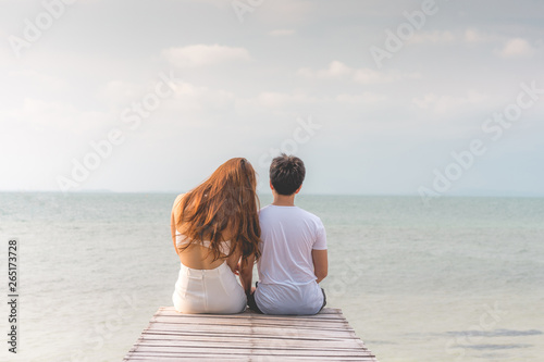 Back of view Vacations of romantic couple in love sitting on pier together seen beautiful sea and beach feeling so happiness and romantic in Tropical island in Thailand,Vacations or honeymoon Concept